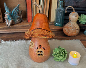 Decorative mushroom fairy house made with a dried gourd. The top still has it's stem, the bottom has carved windows so show candle light. 
